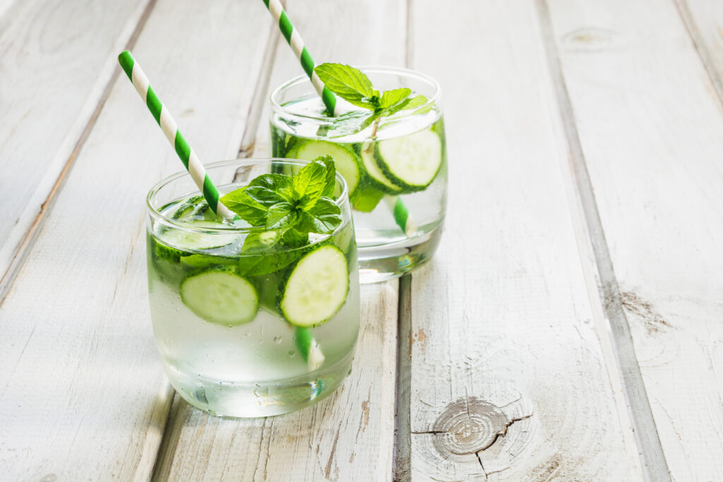 Summer refreshing detox cocktail. Water with cucumber,mint and ice in glass on a white wooden background. Rustic style.